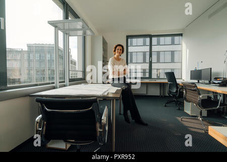 Successful businesswoman sitting on desk in her office Stock Photo