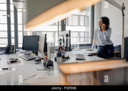 Mature businesswoman sitting o desk in office, talking on the phone Stock Photo