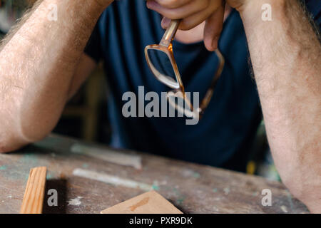 Close-up of man at workbench in workshop holding eyeglasses Stock Photo