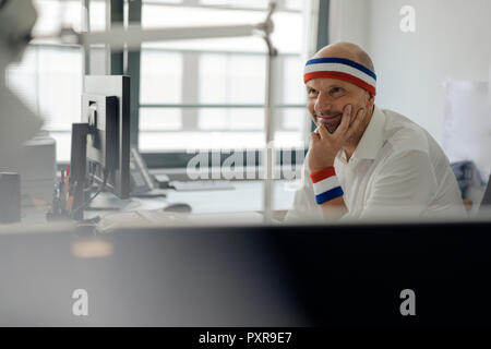Businessman sitting in office, wearing sweat bands Stock Photo