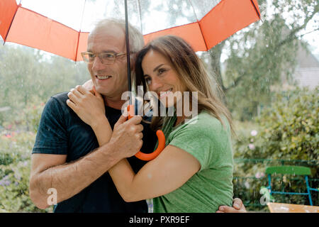 Smiling mature couple standing in rain under umbrella Stock Photo