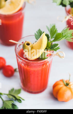 Glasses of fresh spicy tomato juice with cellery garnished with lemon slice, green olive and parsley Stock Photo