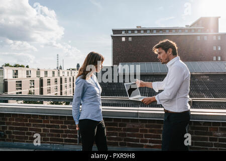 Business people standing on balcony, discussing, using laptop Stock Photo
