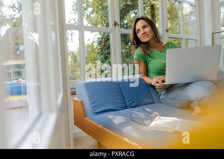 Smiling mature woman sitting on couch at home with laptop Stock Photo