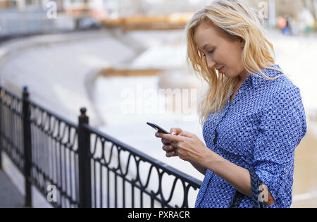 Blond woman using smartphone on a street Stock Photo