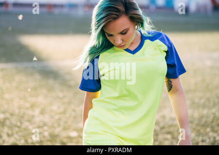 Portrait of young woman in jersey on football ground looking down Stock Photo