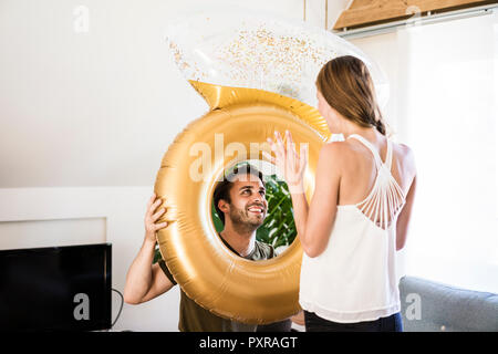 Smiling man looking at girlfriend through large inflatble ring at home Stock Photo