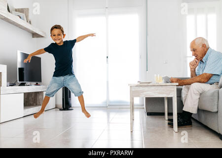 Grandfather sitting on the couch looking at tablet while his grandson jumping in the air Stock Photo