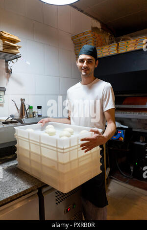 Portrait of smiling pizza baker with boxes of dough in kitchen Stock Photo