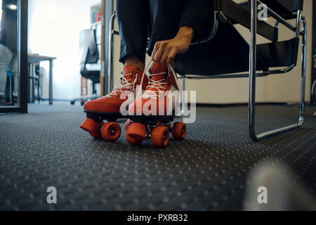 Mature businesswoman sitting in office, putting on roller skates Stock Photo