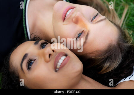 Two girlfriends relaxing in a park, lying on grass Stock Photo