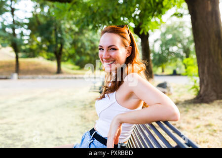Portrait of laughing redheaded woman sitting on bench in a park Stock Photo