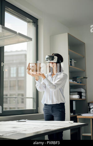 Woman holding architectural model of house, using VR glasses Stock Photo