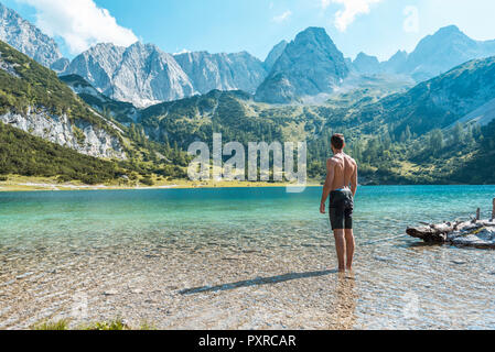 Austria, Tyrol, Young man at Lake Seebensee standing ankle deep in water Stock Photo