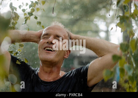 Smiling mature man enjoying summer rain in garden Stock Photo