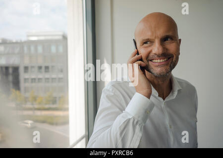 Smiling businessman standing in his office, talking on his mobile phone Stock Photo