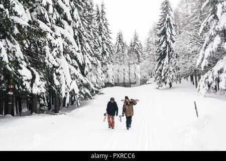 Italy, Modena, Cimone, couple with skiers and snowboard walking in winter forest Stock Photo