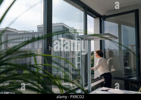 Businesswoman standing in office, looking out of window Stock Photo