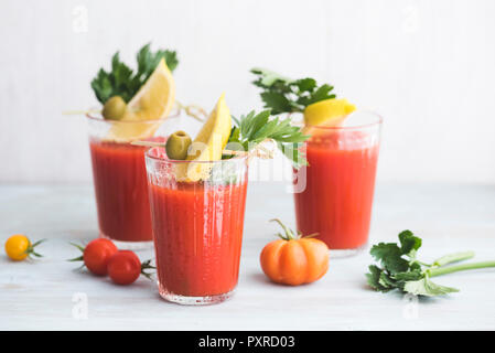 Glasses of fresh spicy tomato juice with cellery garnished with lemon slice, green olive and parsley Stock Photo