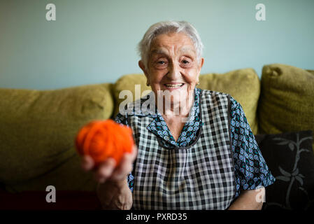 Portrait of smiling senior woman with ball of wool sitting on the couch at home Stock Photo