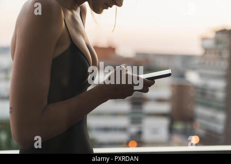 Close-up of young woman wearing black dress using cell phone on balcony Stock Photo