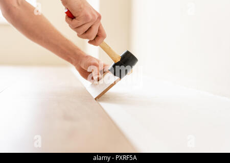 Strikes with a soft hammer on the part with a lock, for fixing. Installing laminate flooring fitting the next piece - focus on hand. Man laying laminate flooring Stock Photo