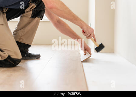 Strikes with a soft hammer on the part with a lock, for fixing. Installing laminate flooring fitting the next piece - focus on hand. Man laying laminate flooring Stock Photo