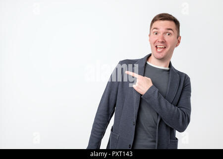 Handsome pensive guy with good-looking hairstyle looking aside and pointing with index finger. Copy space. Stock Photo