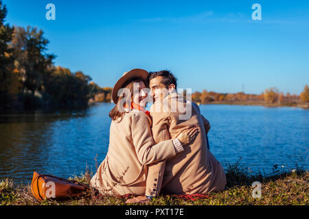 Young couple in love chilling by autumn lake. Happy man and woman enjoying nature and hugging. Romantic date Stock Photo