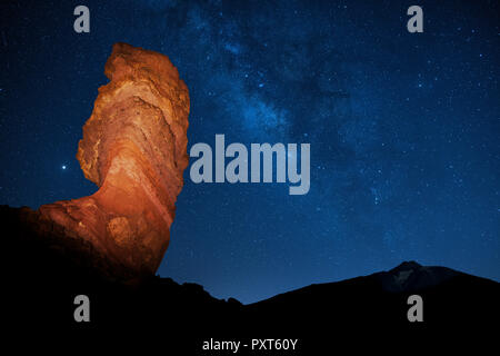 Illuminated Roque Cinchado in front of Pico del Teide with starry sky, Milky Way, night scene at new moon, Los Roques de Garcia Stock Photo