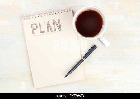 A photo of a spiral notebook with the word Plan, with a cup of coffee and a pen, shot from above on a light wooden desk with copy space Stock Photo
