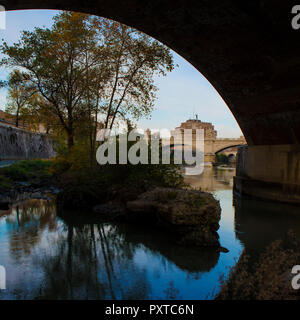 A view of the Castel Sant'Angelo in Rome looking along the River Tiber,under the arch of a bridge. In the foreground trees are reflected in the water Stock Photo