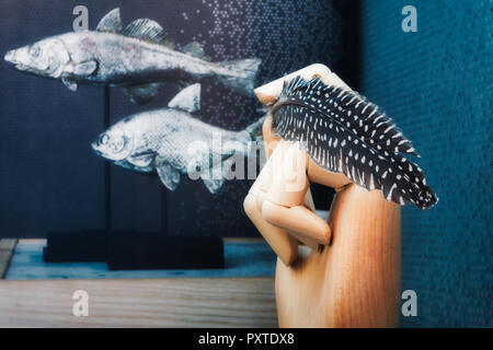 Articulated wooden hand delicately holding a feather on a blue background with fish Stock Photo