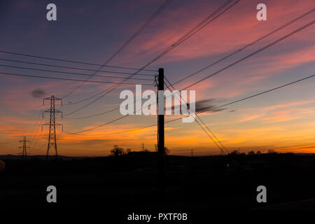Colourful sunset with electricity pylons and wires silhouetted against the sky. Carr, County Down, N.Ireland. Stock Photo