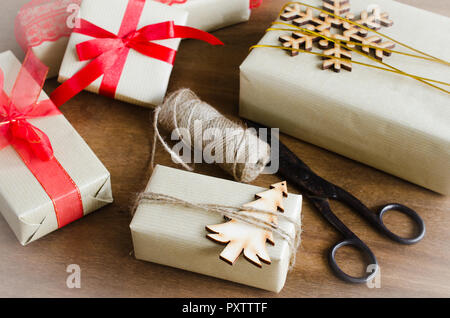 Packing Christmas Gifts. Top View of Festive Boxes in Brown Paper Decorated with Red Bow Ribbon, Christmas Tree and Jute on Wooden Table. Selective Fo Stock Photo