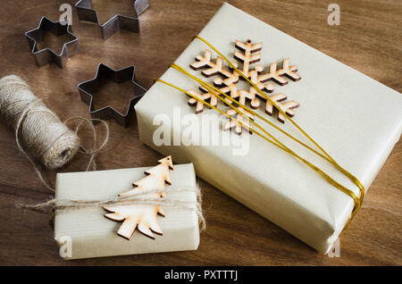 Christmas Gifts. Top View of Festive Boxes in Brown Paper Decorated with Wooden Snowflake, Christmas Tree and Jute on Wooden Table. Stock Photo