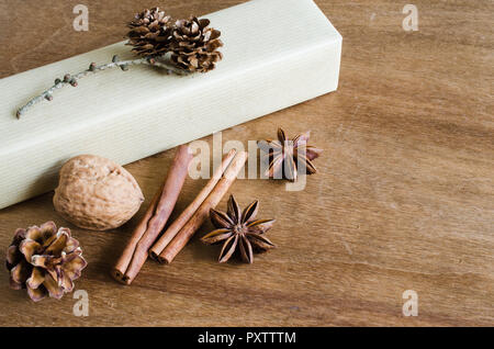 Christmas Gift Box in Rustic style Decorated with Pine Cones, Cinnamon, Walnuts on Wooden Background. Selective Focus. Copy Space. Stock Photo