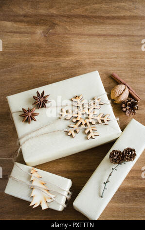 Christmas Gift Boxes in Rustic style Decorated with Wooden Snowflake and Xmas Tree, Linen Cord, Cinnamon, Pine Cones, Walnuts on Wooden Background. To Stock Photo