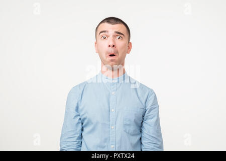 Portrait of fearful young man in blue shirt keeping mouth wide open, feeling stressed Stock Photo