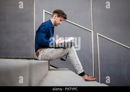 Businessman sitting on stairs outdoors taking notes Stock Photo