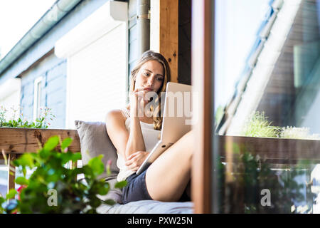 Smiling woman on balcony using laptop Stock Photo