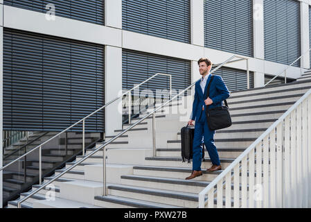 Smiling businessman with baggage in the city walking down stairs Stock Photo
