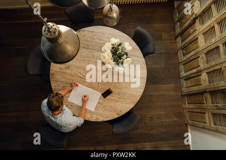 Mature man sitting at a round table, drawing with coloured pencils, overhead view Stock Photo