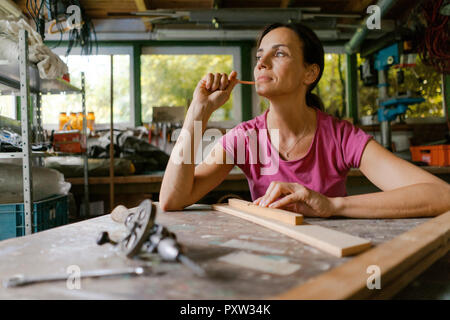 Mature woman at workbench in her workshop thinking Stock Photo