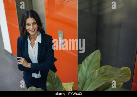 Portrait of a successful businesswoman, standing in front of elevator, with arms crossed Stock Photo