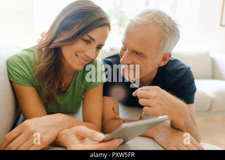 Smiling mature couple lying on couch at home sharing tablet Stock Photo