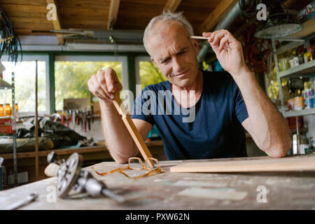 Mature man at workbench in his workshop thinking Stock Photo