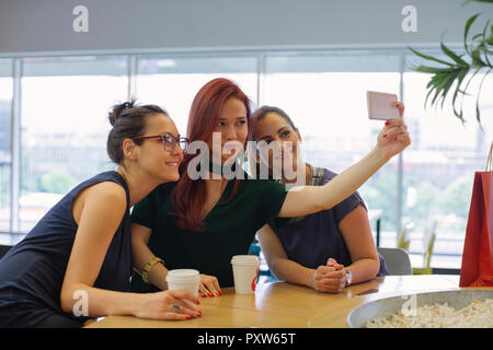 Girl friends on a shopping spree meeting in a coffee shop, taking selfies Stock Photo