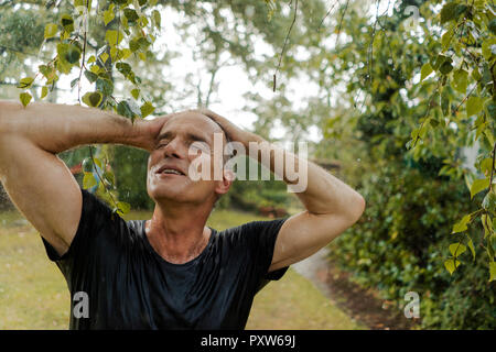 Smiling mature man enjoying summer rain in garden Stock Photo