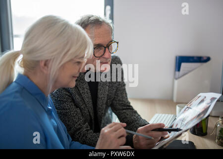Two senior colleagues working together at desk in office examining photos Stock Photo
